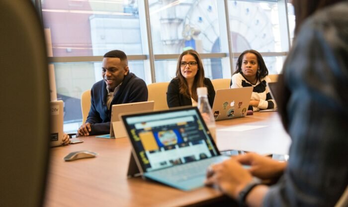 A diverse group of professionals working together on laptops in a modern office meeting room.